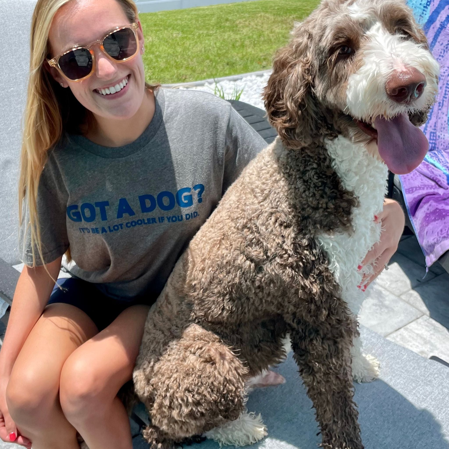 Young female sitting poolside with her Doodle Dog. The female is wearing a funny deep heather gray Luv the Paw t-shirt that says "Got a Dog? It'd be a lot cooler if you did".