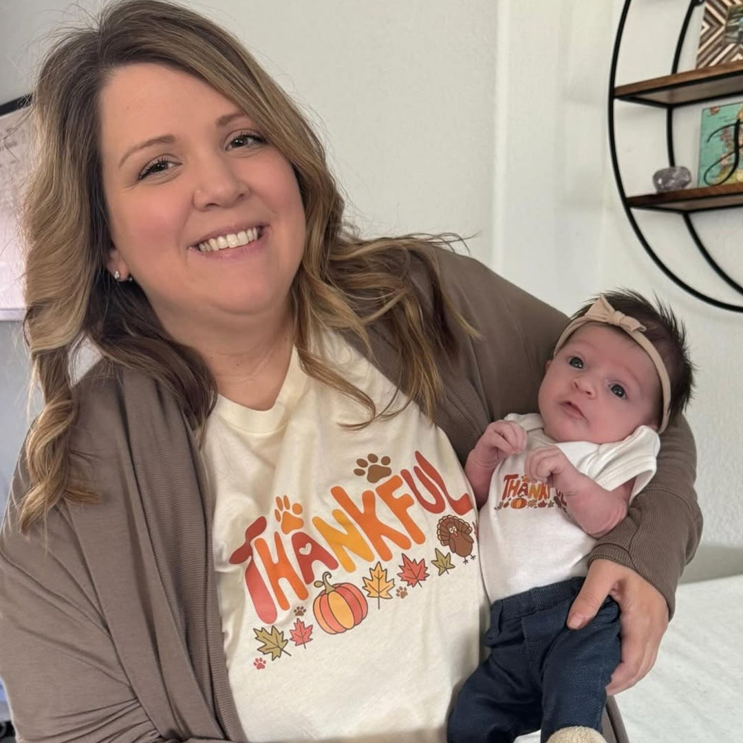 Smiling woman in a cream Thankful t-shirt holding a baby