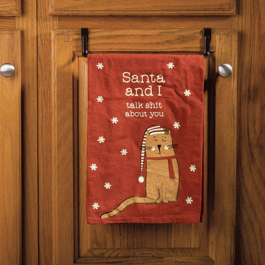 Funny red Christmas kitchen towel with cat wearing Santa hat and text “Santa and I talk shit about you” hanging on cabinet door.