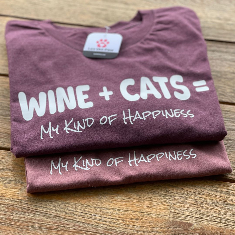 Two folded shirts on a wooden table that say "Wine+Cats=My Kind of Happiness"