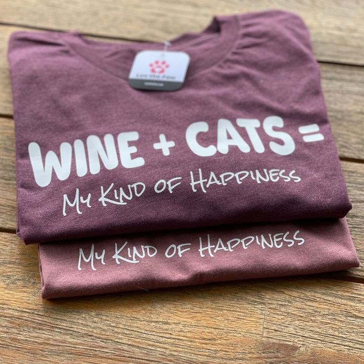 Two folded shirts on a wooden table that say "Wine+Cats=My Kind of Happiness"