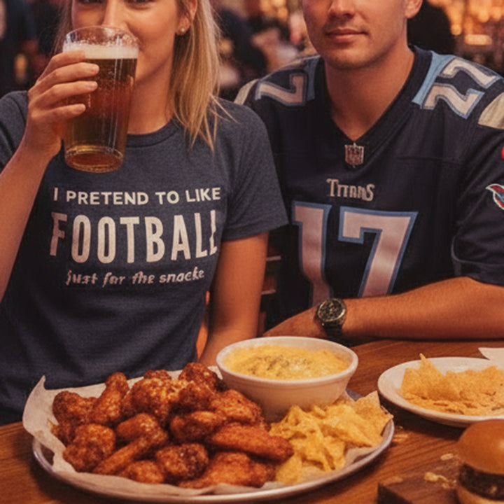Two people sitting at a table with food and drinks, one wearing a 'I Pretend to Like Football' shirt.